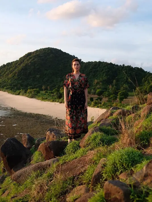 Tampil natural menggunakan dress berwarna hitam dengan motif bunga-bunga berwarna merah, wanita berusia 29 tahun ini berdiri di sebuah bukit bebatuan dipenuhi rumput hijau di Lombok. Kecantikannya tak pernah pudar. (Liputan6.com/IG/@raisa6690)