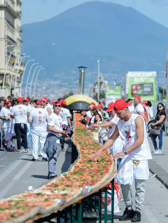 Tahap akhir pembuatan pizza sepanjang 1 mil untuk pecahkan rekor dunia di pinggir Laut Naples, Italia, 18 Mei 2016. Pizza terpanjang itu dibuat menggunakan 2.000 kg tepung, 1.6000 kg tomat, 2.000 kg mozzarella dan 200 liter minyak. (Mario LAPORTA/AFP)