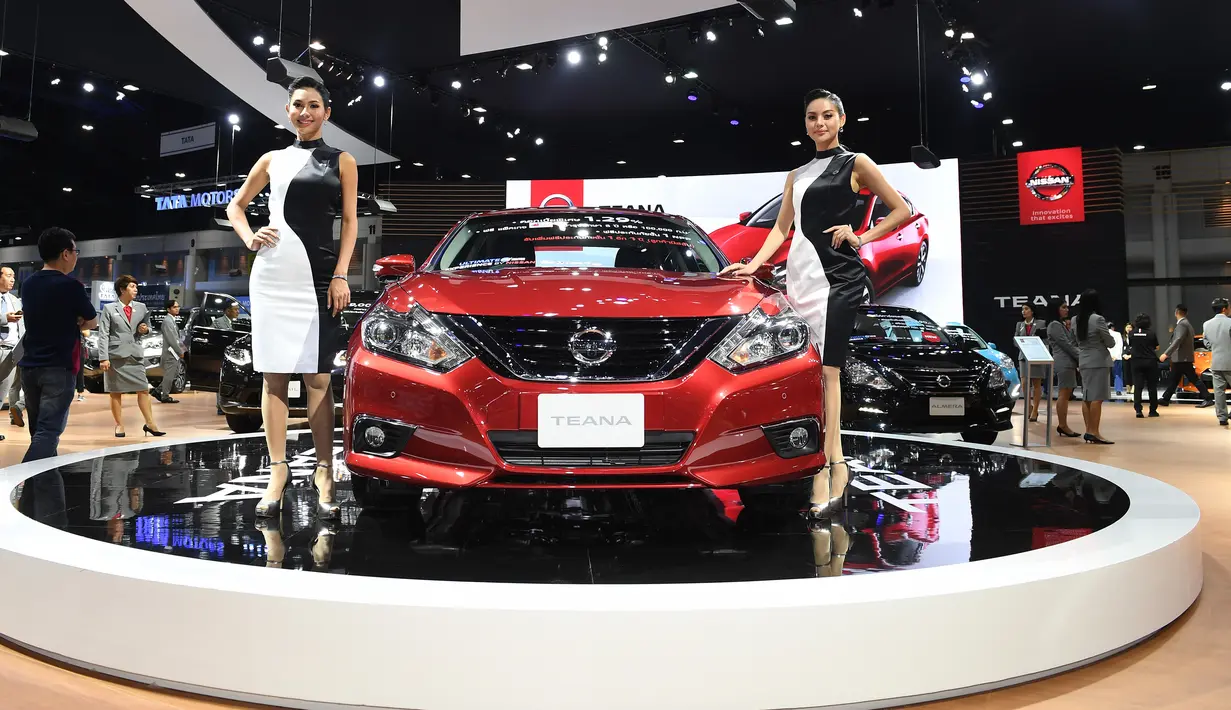 Dua model berpose di samping mobil Nissan Teana 2019 selama Thailand International Motor Expo di Bangkok (29/11). Thailand International Motor Expo bertema “Enjoy Driving! Before Driverless Era”.  (AFP Photo/Lillian Suwanrumpha)
