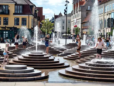 Anak-anak mendinginkan diri dengan bermain di air mancur saat gelombang panas menerjang Eropa di Toldbod Plads, Aalborg, Denmark, Rabu (24/7/2019). Eropa Barat dilanda gelombang panas yang hebat minggu ini. (Henning Bagger/Ritzau Scanpix via AP)