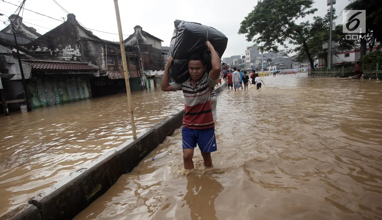 Warga berjalan melintasi banjir membawa barang mereka di Jalan Jatinegara Barat, Jakarta Timur, Selasa (6/2). Akibat banjir ini ruas jalan tersebut tidak dapat dilalui kendaraan. (Liputan6.com/Arya Manggala)
