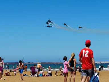 Para pengunjung pantai saat menyaksikan aksi tim aerobatik Angkatan Udara Spanyol, Patrulla Aspa yang bermanuver menggunakan helikopter di San Lorenzo, Gijon, Spanyol, Minggu (24/7). (REUTERS/Eloy Alonso)