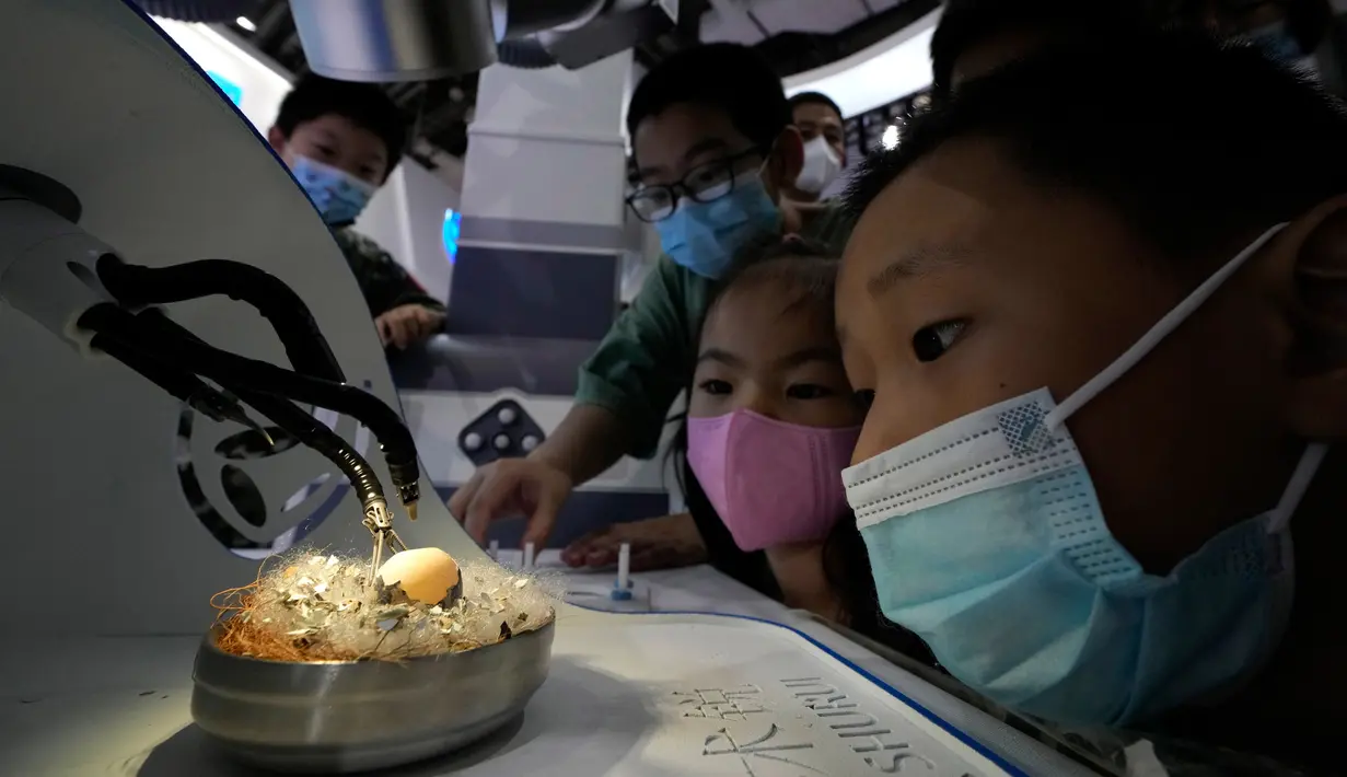 Anak-anak yang memakai masker menyaksikan robot bedah menunjukkan ketangkasannya dengan mengeluarkan cangkang dari telur saat Konferensi Robot Dunia di Yichuang International Conference and Exhibition Centre, Beijing, China, 19 Agustus 2022. (AP Photo/Ng Han Guan)