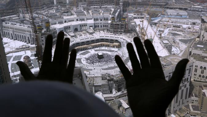 Umat Muslim berdoa dari sebuah hotel yang menghadap ke Kakbah di Masjid al-Haram, Makkah, Arab Saudi, Rabu (4/3/2020). Pemerintah Kerajaan Arab Saudi melalui Wakil Menteri Kesehatan Abdel-Fattah Mashat melarang sementara penduduknya untuk melaksanakan ibadah umrah. (AP Photo/Amr Nabil)