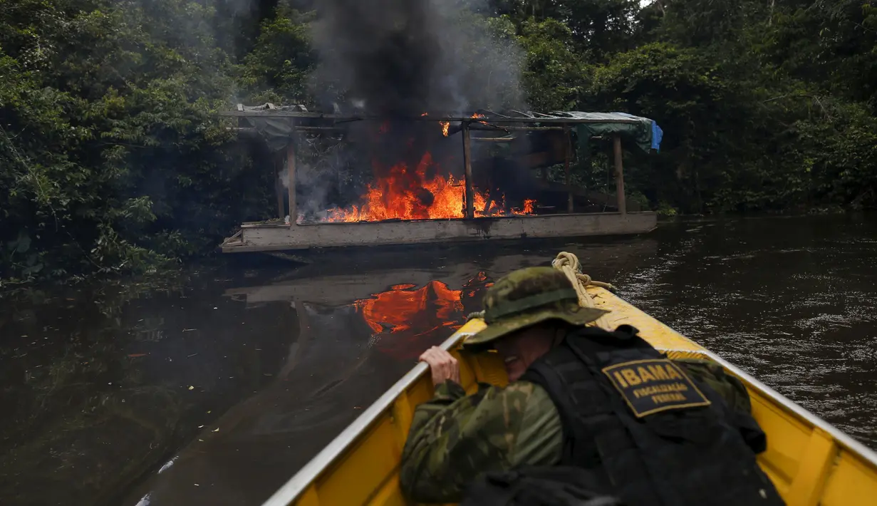 Petugas lingkungan Brasil saat berlindung dari kapal yang dibakar selama operasi terhadap penambangan emas ilegal di perairan hutan hujan Amazon, Roraima, Brasil (16/4). Daerah ini merupakan tempat dimana suku Yanomami tinggal. (REUTERS / Bruno Kelly)