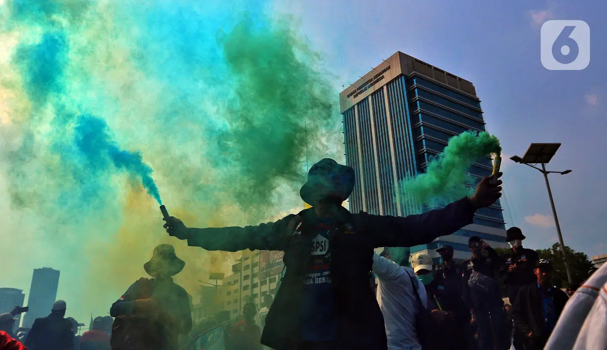 Buruh menyalakan suar saat melakukan unjuk rasa di depan Gedung DPR, Jakarta, Rabu (10/8/2022). Dalam aksi tersebut mereka menuntut agar pemerintah menghapus Omnibus Law. (Liputan6.com/Angga Yuniar)