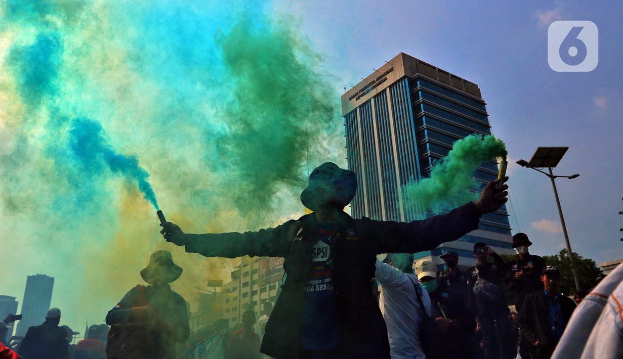 Buruh menyalakan suar saat melakukan unjuk rasa di depan Gedung DPR, Jakarta, Rabu (10/8/2022). Dalam aksi tersebut mereka menuntut agar pemerintah menghapus Omnibus Law. (Liputan6.com/Angga Yuniar)