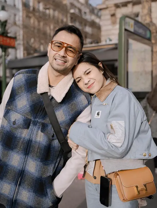 Nagita Slavina berpose mesra dengan sang suami tampil mengenakan outfit yang ditumpuk. Ia tampak menumpuk inner cokelat dengan jaket abu-abu, lalu cropped jacket bernuansa biru muda. Penampilannya ia padukan mengenakan celana jeans dan sling bag cokelat. [Foto: Instagram/raffinagita1717]