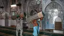Umat Muslim membawa karpet sajadah dari aula utama masjid menyusul pembatasan baru pemerintah baru menjelang bulan suci Ramadan di Rawalpindi, Pakistan, Senin (5/4/2021). Sesuai pedoman, barisan orang yang salat harus sejajar sehingga ada jarak enam kaki antarindividu. (Aamir QURESHI/AFP)