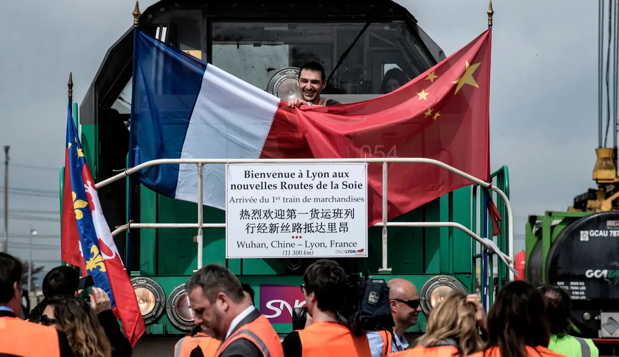 Seorang pria memegang bendera Perancis dan Cina di atas kereta barang di stasiun Saint-Priest, Lyon, Prancis, (21/4). Untuk pertama kali, kereta barang yang mengangkut 41 kontainer dari China tiba di Prancis. (AFP PHOTO/JEFF PACHOUD)