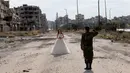 Salah satu momen dramatis saat seorang tentara Suriah, Hassan Youssef (27) memberi hormat kepada pengantin wanita, Nada Merhi (18), dengan latar belakang pemandangan tandus kota Homs yang menjadi medan perang di Suriah, 5 Februari 2016. (JOSEPH EID/AFP)