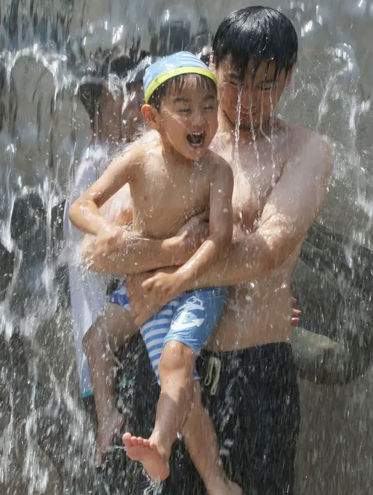 Seorang ayah menggendong anaknya saat bermain air di sebuah taman, Tokyo, (16/7). Badan Meteorologi mengatakan gelombang panas terus berlanjut di wilayah metro ketika suhu naik mencapai 35 derajat Celcius (95 derajat Fahrenheit). (AP Photo/Koji Sasahara)