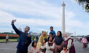 Warga berswafoto saat berwisata di kawasan Monumen Nasional (Monas), Jakarta, Sabtu (5/4/2025). (Liputan6.com/Herman Zakharia)
