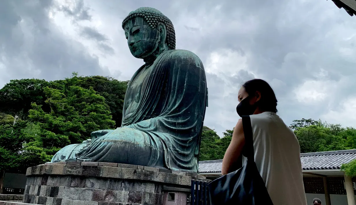 Seorang perempuan bermasker mengunjungi The Great Buddha atau yang biasa disebut Kamakura Daibutsu di kuil Kotoku-in di Kamakura, Prefektur Kanagawa, Jepang, Sabtu (20/6/2020). Patung Buddha dari perunggu yang menjulang dengan tinggi 13,35 meter ini didirikan tahun 1252. (Behrouz MEHRI/AFP)