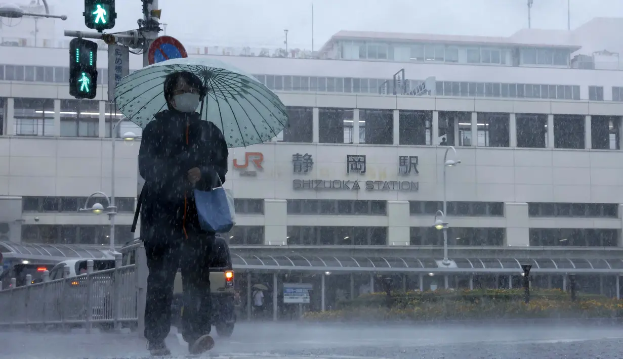 Seseorang berjalan di tengah hujan di depan sebuah stasiun di Shizuoka, sebelah barat Tokyo, Sabtu (13/8/2022). Badai Tropis Meari mengeluarkan hujan lebat di barat daya Jepang saat menuju ke utara menuju ibu kota Tokyo, menurut pejabat cuaca Jepang. (Kyodo News via AP)