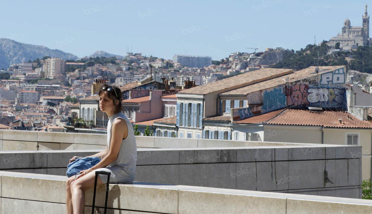 Seorang wanita duduk dengan latar belakang suasana kota di Marseille, Prancis, Minggu (3/7/2016). Marseille merupakan daerah pesisir di selatan Prancis dengan pesona keindahan alam. (Bola.com/Vitalis Yogi Trisna)