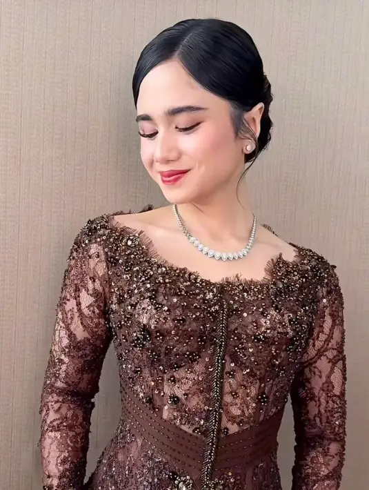 Ia tampil dalam balutan kebaya klasik bernuansa cokelat mahogani yang memancarkan kesan elegan sekaligus hangat. Kebaya rancangan Fadlan Indonesia ini dipenuhi detail brokat dan payet yang memberikan efek berkilau halus, menciptakan tampilan mewah tanpa terasa berlebihan.