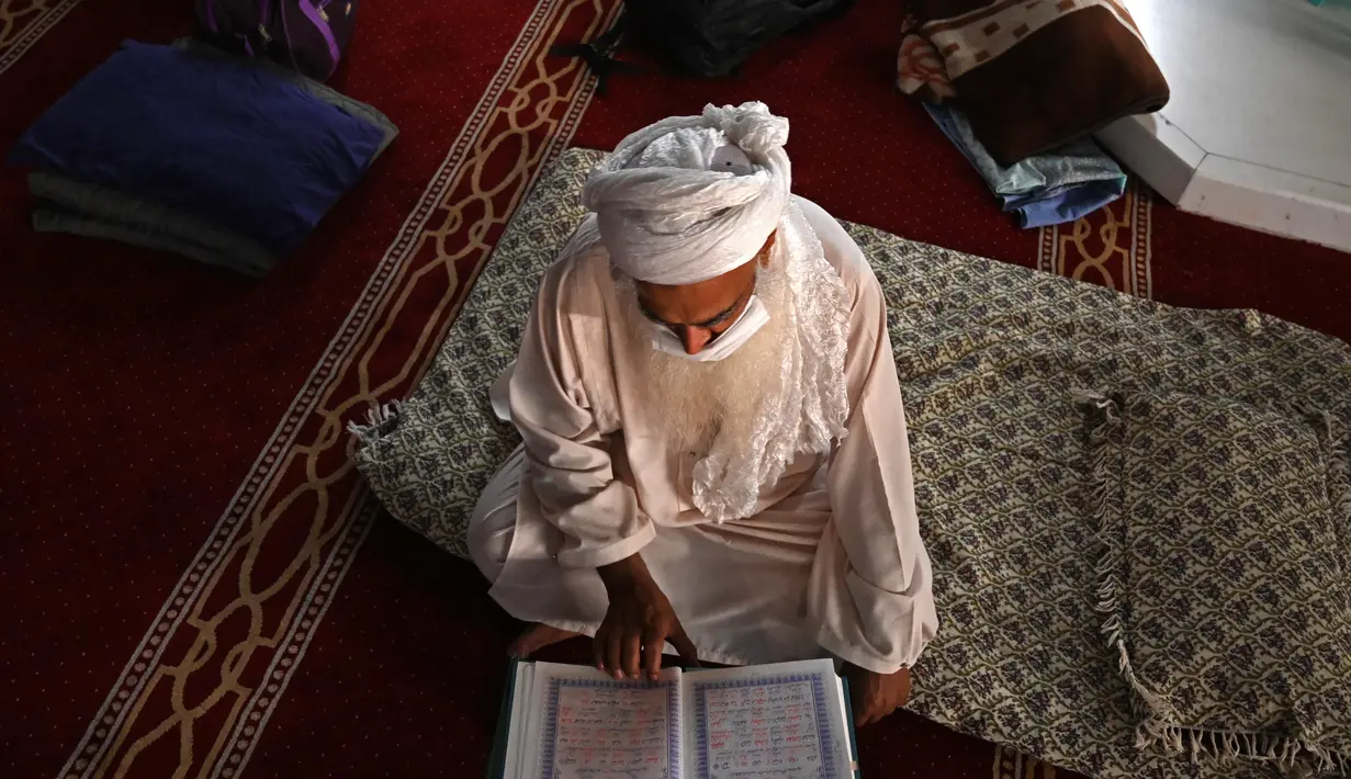 Seorang pria Muslim yang mengenakan masker wajah membaca Alquran di Masjid Agung Faisal pada awal Itikaf, di sebuah masjid untuk pria selama bulan suci Ramadhan di Islamabad (3/5/2021). (AFP/Aamir Qureshi)