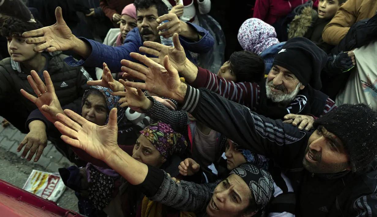 Warga menerima bantuan dari relawan di Antakya, Turki selatan, Rabu, 8 Februari 2023. Tim penyelamat yang bekerja keras sepanjang malam hingga Rabu, menarik lebih banyak jenazah dari puing-puing ribuan bangunan yang runtuh di Turki dan Suriah akibat bencana gempa bumi. (AP Photo/Khalil Hamra)