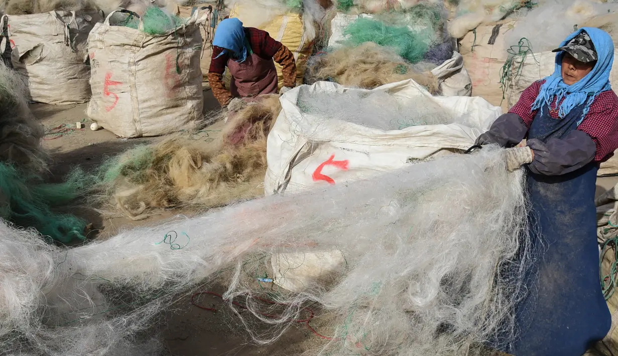 Para nelayan membersihkan jaring ikan yang dibuang untuk didaur ulang di sebuah desa di Lianyungang, di provinsi Jiangsu timur China (17/3/2021). Daur ulang jaring ikan tersebut akan dibuat palet nilon. (STR/AFP/China Out)