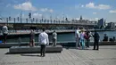 Orang-orang berdiri di dermaga Golden Horn, di depan Jembatan Galata di Istanbul, Turki pada Senin (17/5/2021). Pemerintah Turki mencabut lockdown atau penguncian penuh selama 17 hari untuk mengekang lonjakan infeksi virus corona COVID-19. (OZAN KOSE / AFP)