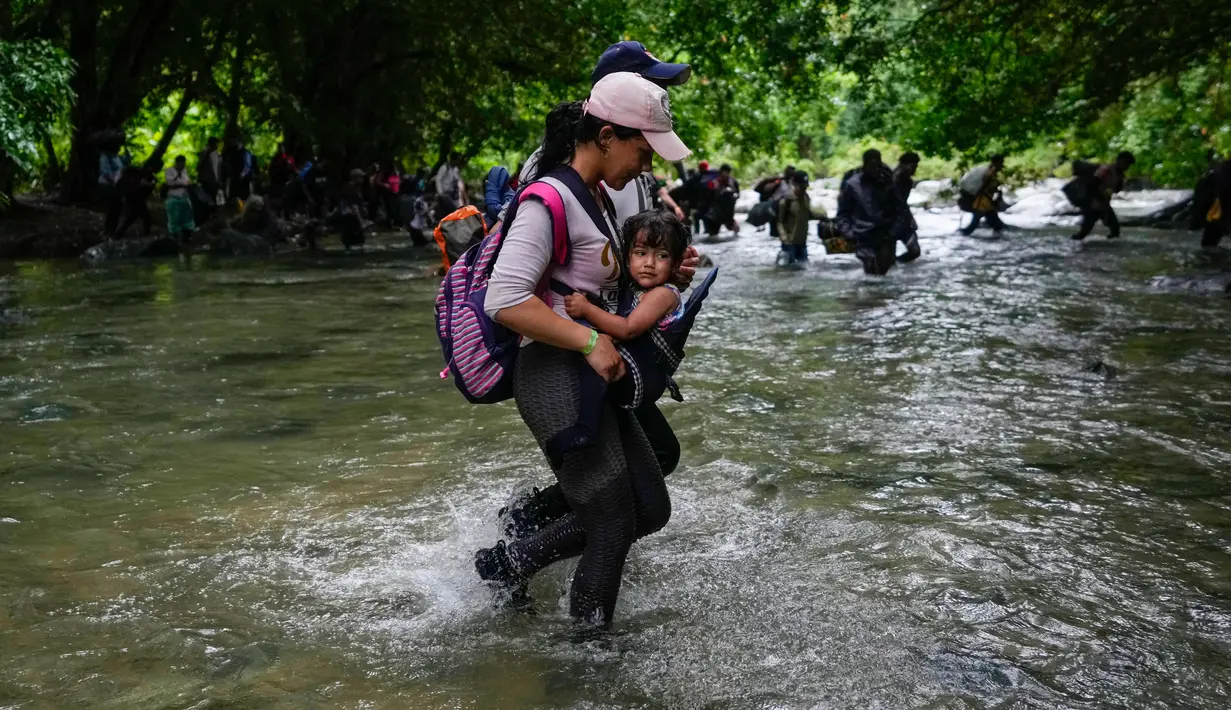 Seorang migran Haiti membawa seorang anak melintasi Celah Darien dari Kolombia ke Panama Sabtu, (15/10/2022). Perjalanan Kelompok Imigran tersebut berharap mencapai Amerika Srikat (AS).(Fernando Vergara/AP)