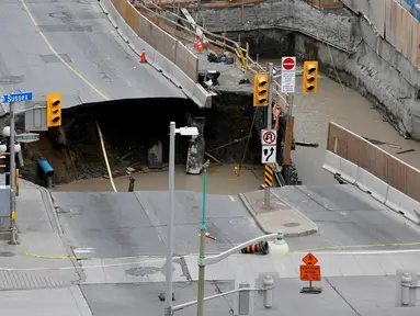 Pekerja mengamati sebuah sinkhole besar yang menganga di Rideau Street, Ottawa, Kanada, Rabu (8/6). Area tersebut berlokasi di daerah yang sedang dilakukan penggalian dan telah ditutup untuk lalu lintas semua kendaraan bermotor. (REUTERS/Chris Wattie)