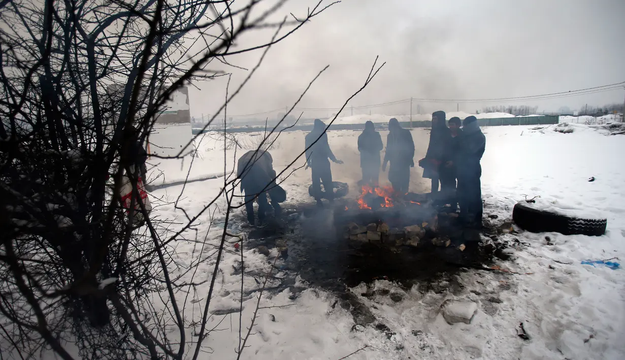 Sejumlah imigran menghangatkan diri di dekat perapian di kamp pengungsian di Belgrade, Serbia (11/1). Mereka harus bertahan hidup dibawah salju dingin dengan suhu -15 derajat Celcius. (AP Photo/Darko Vojinovic)