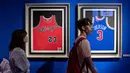 Pengunjung melihat jersey Michael Jordan (kiri) dan Allen Iverson (kanan) yang dipamerkan dalam pameran NBA (National Basketball Association) di Beijing, China, Senin (19/8/2019). (NICOLAS ASFOURI/AFP)