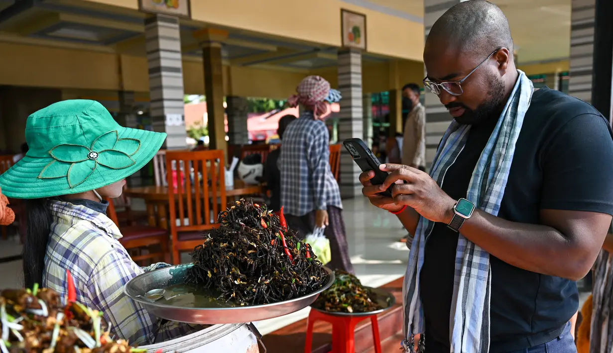 Seorang turis mengambil gambar tarantula goreng di kota Skun di provinsi Kampong Cham pada 15 Januari 2023. Di wilayah Skun, Provinsi Kampong Cham, yang kerap dijuluki "Spiderville", para turis dapat menyaksikan bagaimana hewan itu digoreng dan disantap. (Photo by TANG CHHIN SOTHY / AFP)
