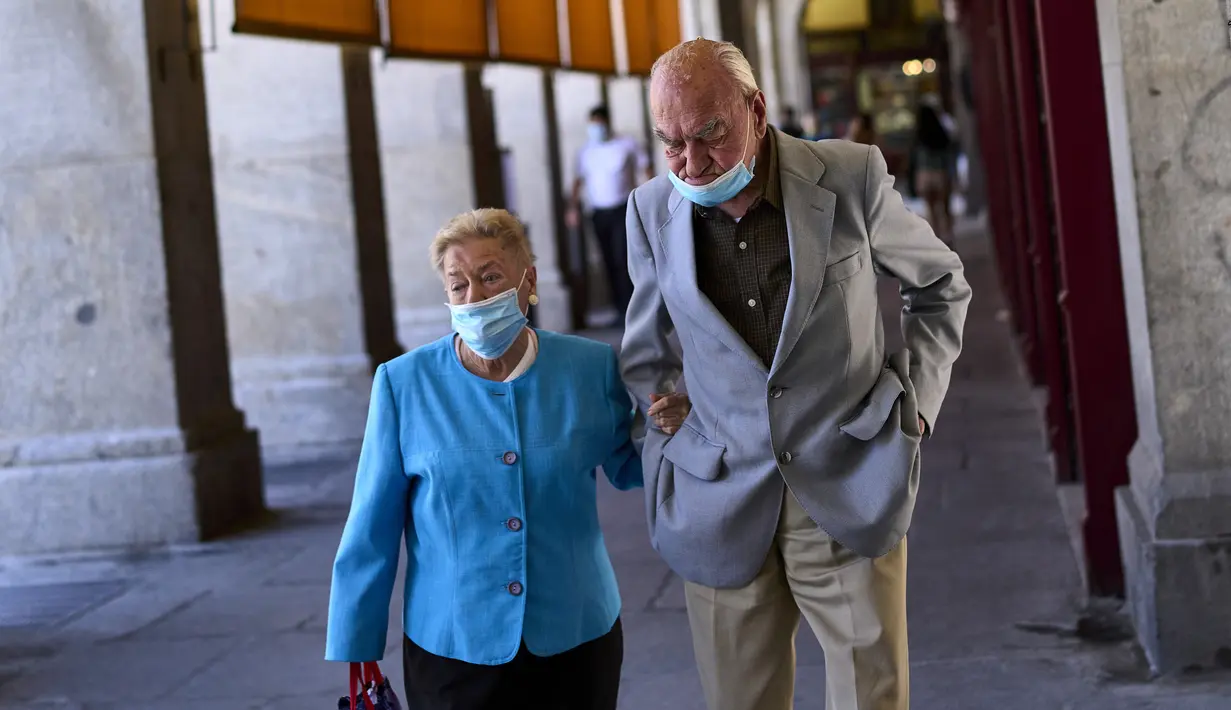 Pasangan yang mengenakan masker berjalan di sepanjang jalan di Madrid, Spanyol, Kamis (24/6/2021). Spanyol melonggarkan aturan pandemi COVID-19, mengizinkan orang berhenti mengenakan masker di luar ruangan dan mengizinkan penggemar olahraga kembali ke dalam stadion.  (AP Photo/Manu Fernandez)