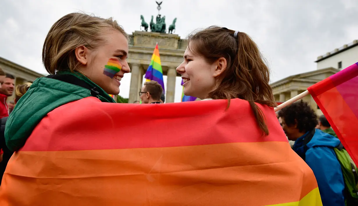 Dua wanita berselimut bendera pelangi saat demontrasi kaum LGBT di depan Gerbang Brandenburg di Berlin (30/6). Sebanyak 393 anggota parlemen Jerman menyetujui pernikahan sesama sejenis, dan 226 anggota lainnya menolaknya. (AFP Photo/Tobias Schwarz)