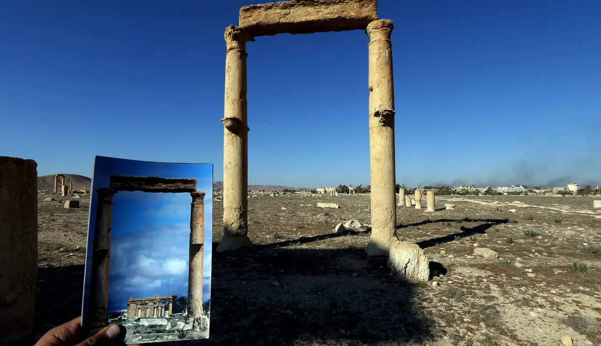 Fotografer bernama Joseph Eid memegang foto Temple of Baal Shamin yang diambil pada tanggal 14 Maret 2014 di depan sisa-sisa kuil bersejarah setelah dihancurkan oleh ISIS pada September 2015 di kota kuno Palmyra, Suriah, 31 Maret 2016. (Joseph EID/AFP)