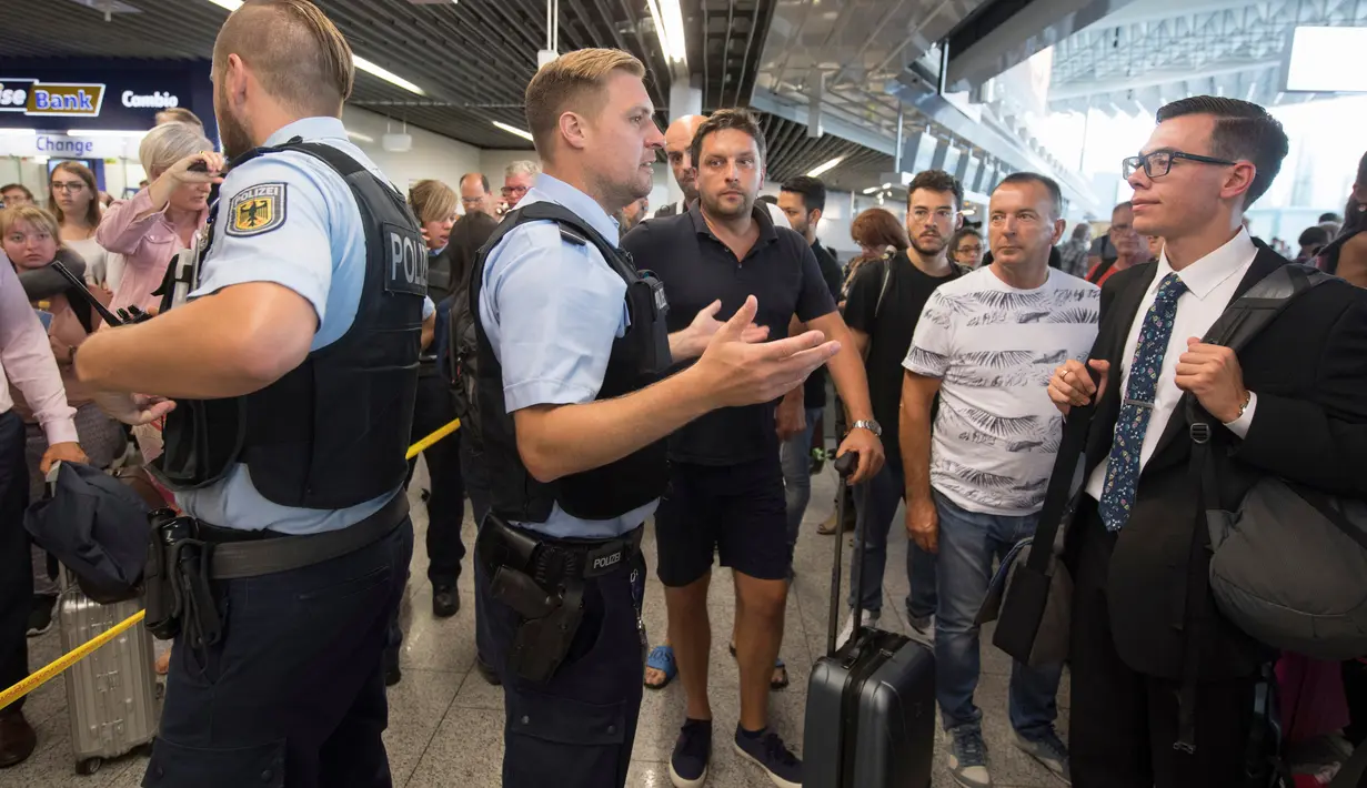 Petugas kepolisian memberi penjelasan kepada calon penumpang di aula terminal 1 Bandara Frankfurt, Jerman, Selasa (7/8). Sejumlah penerbangan harus dibatalkan setelah seorang yang tak dikenal menyusup melewati pos pemeriksaan. (Boris Roessler/dpa via AP)