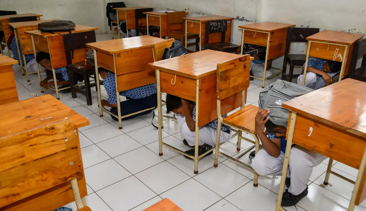 Sejumlah siswa berlindung di bawah meja saat simulasi bencana gempa dan tsunami di sebuah sekolah di Banda Aceh, Aceh, Rabu (9/10/2019). Para siswa dibekali wawasan tanggap darurat bencana dan pemberian pertolongan pertama pada korban gempa. (Photo by CHAIDEER MAHYUDDIN / AFP)