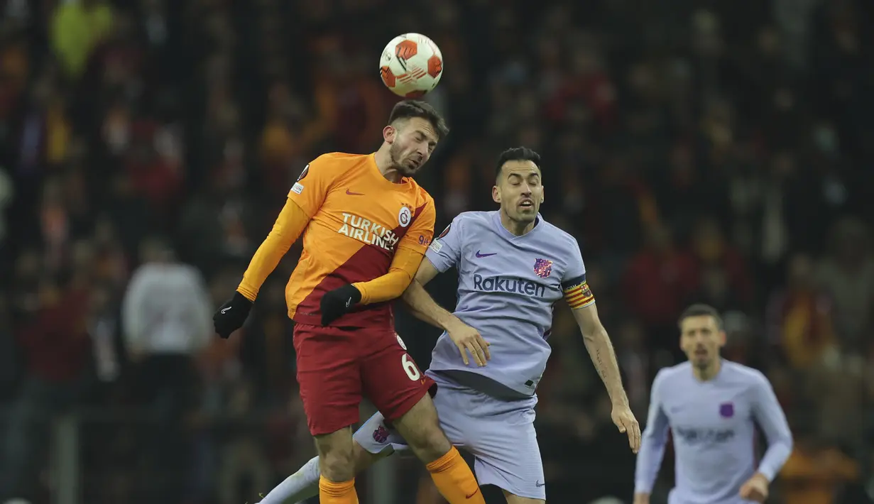 Penyerang Galatasaray Halil Dervisoglu dan gelandang Barcelona Sergio Busquets menyundul bola pada leg kedua 16 besar Liga Europa di NEF Stadyumu, Jumat (18/3/2022) dini hari WIB. Hasil Galatasaray vs Barcelona berakhir dengan skor 1-2. (AP Photo)