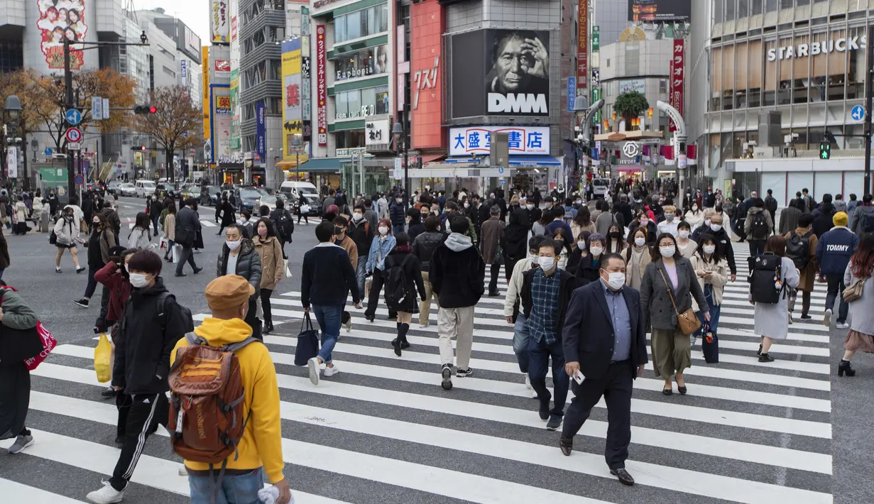 Orang-orang, yang mengenakan masker wajah, berjalan melintasi persimpangan di Tokyo (11/12/2020). Tokyo melaporkan 621 kasus COVID-19 baru pada hari Sabtu, 12 Desember, menetapkan level tertinggi baru di ibu kota Jepang. (AP Photo / Hiro Komae)