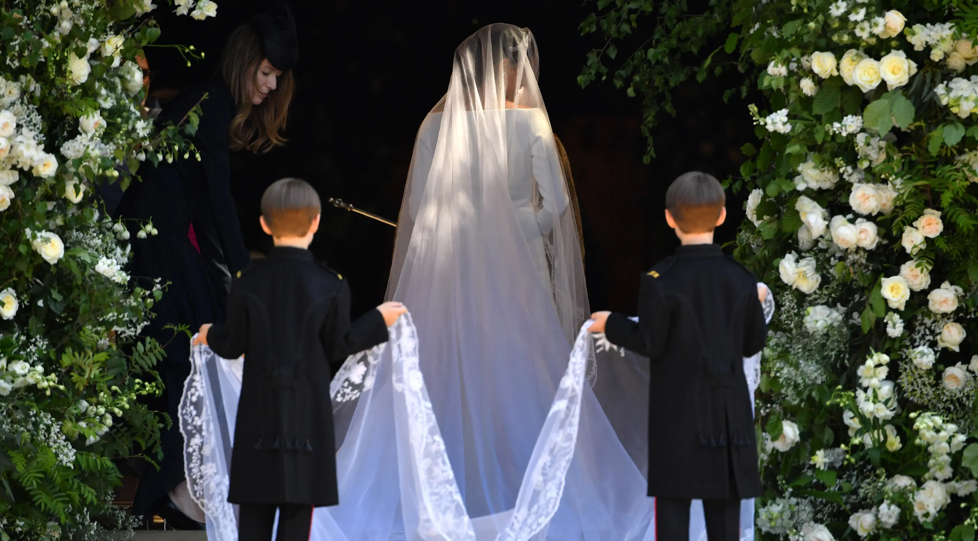 Dua bocah memegang gaun putih panjang Meghan Markle saat akan melangsungkan upacara pernikahan dengan Pangeran Harry di St George's Chapel, Kastil Windsor, Windsor, Inggris, Sabtu (19/5). (Andrew Matthews/POOL/AFP)