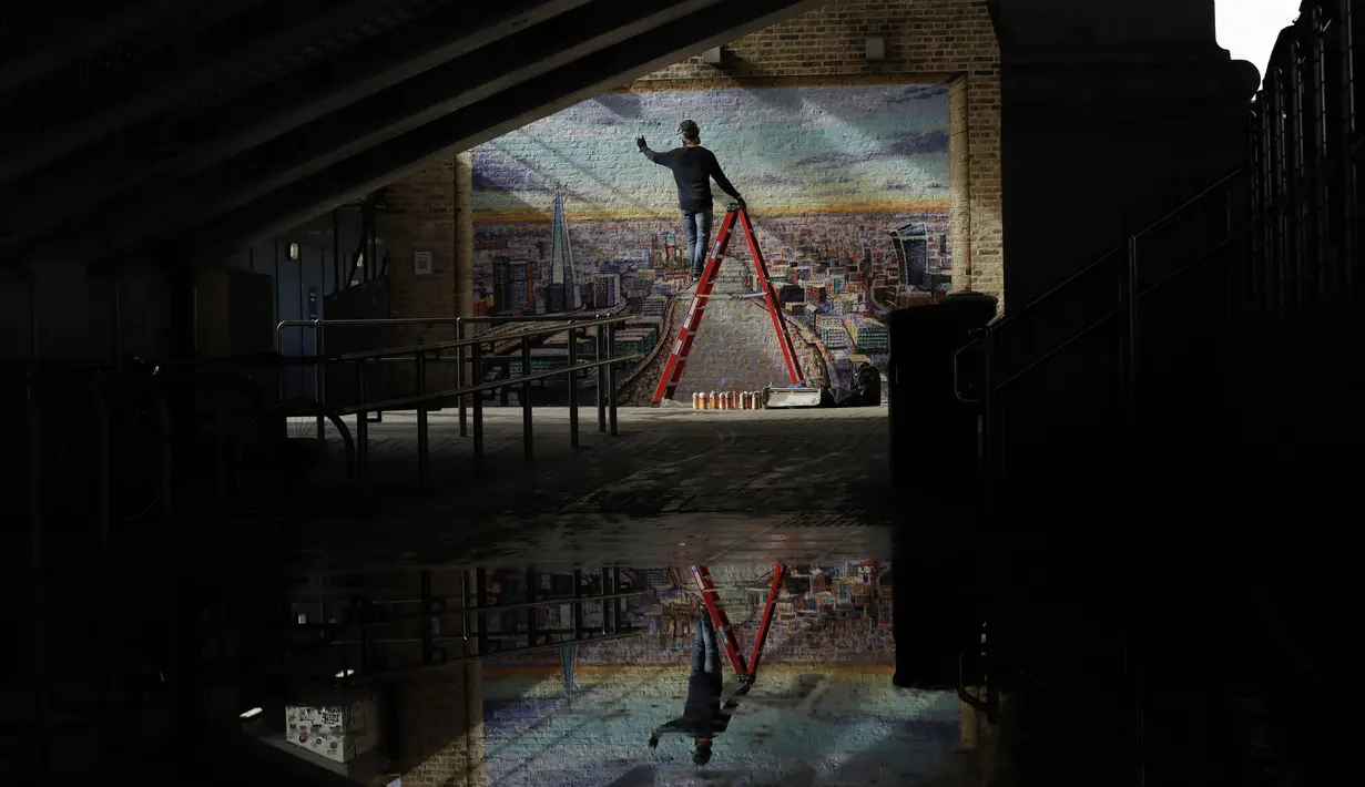 Seniman jalanan Australia James Cochran memberikan sentuhan akhir pada mural lanskap kota London di dinding Network Rail oleh Blackfriars Station, London (5/10/2020). Cochran membutuhkan waktu enam hari untuk melukis lanskap kota London dalam kondisi basah dan hujan. (AP Photo/Matt Dunham)