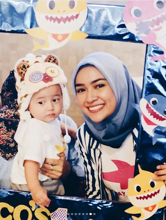 Bintang sinetron mengenakan kaos putih bertuliskan Mommy Shark dan gambar hiu merah. Aryani memadukannya dengan kemeja bergaris lengan panjang. (Instagram/aryanifitriana24)