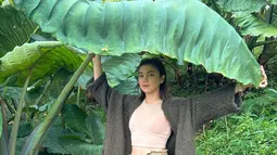 Di hutan Angela Gilsha, tak takut kehujanan meski tak membawa payung. Ia memanfaatkan daun ukuran besar untuk melindungi kepalanya. (Foto: Instagram/@angelagilsha)