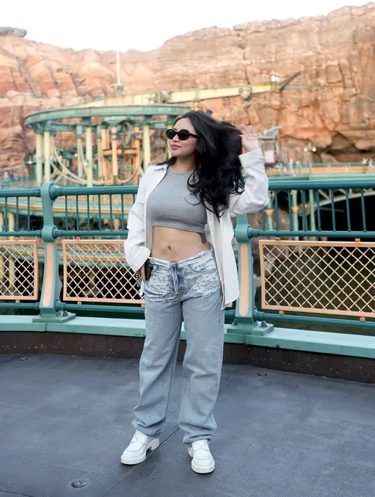 Rachel Vennya dengan outfit pamer perut, siapa takut? Rachel Vennya memilih mengenakan crop top abu-abu, ditumpuk kemeja putih dengan kancing terbuka, sehingga memperlihatkan perutnya yang rata, dipadu celana jeans, dan sneakers putih. Foto: Instagram.
