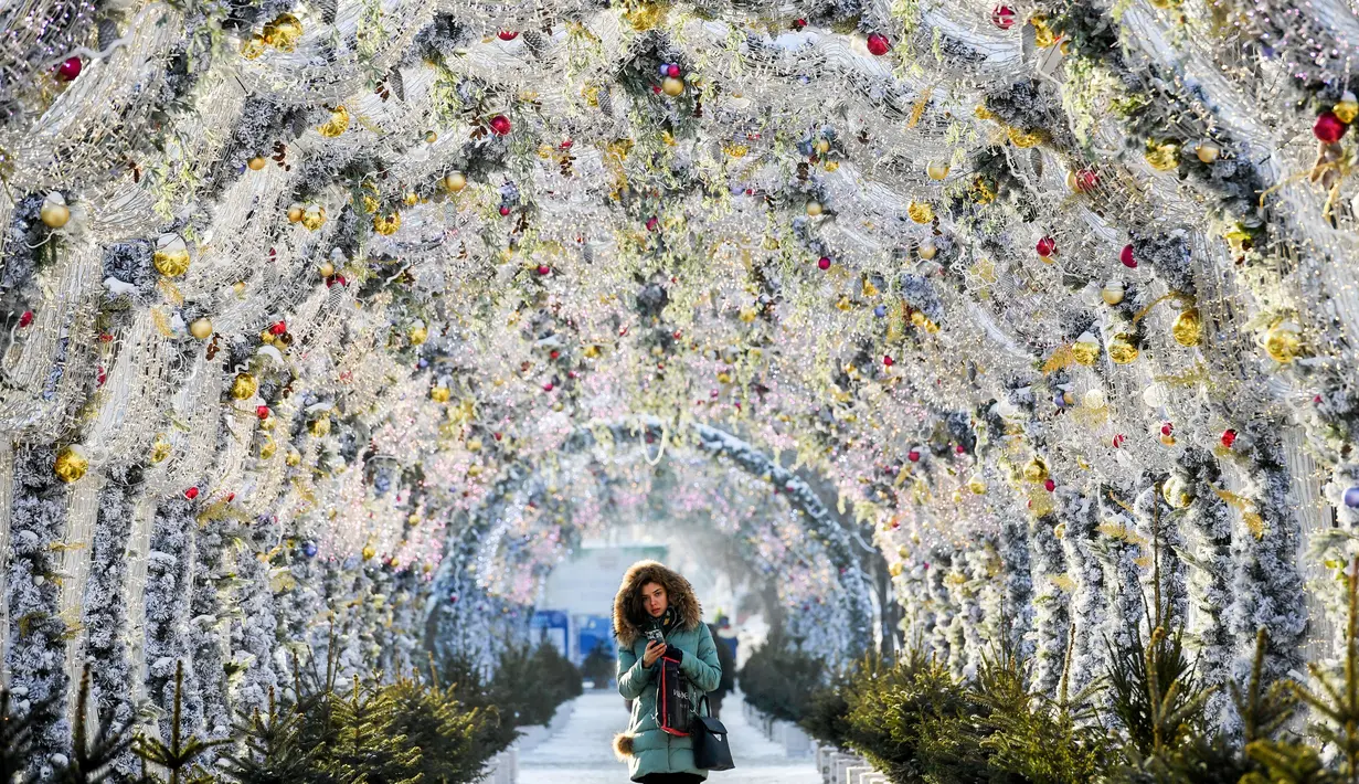 Seorang wanita melintasi terowongan yang dihias dengan lampu-lampu meriah untuk menyamb ut Natal dan Tahun Baru di Moskow, Rusia, Senin (17/12). (Kirill KUDRYAVTSEV/AFP)