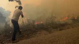 Seorang pria mencoba untuk memadamkan kebakaran hutan ga, di desa Qobayat, di utara provinsi Akkar, Lebanon, Kamis (29/7/2021). Kobaran api telah memaksa beberapa warga untuk meninggalkan rumah mereka. (AP Photo/Hussein Malla)