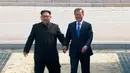 Pemimpin Korea Utara Kim Jong-un dan Presiden Korea Selatan Moon Jae-in berjalan dengan bergandeng tangan melewati Zona Demiliterisasi, Jumat (27/4). Kim dan Moon menuju Rumah Perdamaian untuk pertemuan tingkat tinggi. (Korea Broadcasting System via AP)
