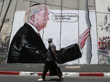 Seorang pria Palestina berjalan didepan grafiti yang menggambarkan Presiden AS Donald Trump di tembok pemisah Israel - Palestina di kota Bethlehem (4/8). Tembok di Tepi Barat ini membentang sepanjang 700 kilometer. (AFP Photo/Musa Al Shaer)