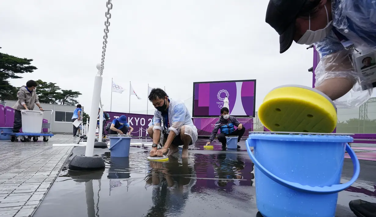 Relawan berusaha mengeluarkan air hujan dari lapangan sebelum latihan menembak putri Olimpiade Tokyo 2020 di Lapangan Menembak Asaka, Tokyo pada 27 Juli 2021. Relawan atau volunteer merupakan salah satu kunci suksesnya suatu perhelatan, tak terkecuali Olimpiade Tokyo 2020 ini. (AP/Alex Brandon)