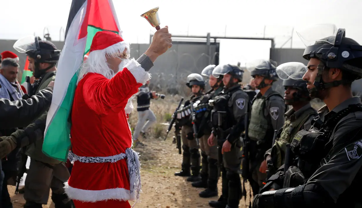 Seorang pengunjuk rasa berkostum Santa Claus menggelar aksi di desa Tepi Barat Bilin dekat Ramallah, Jumat (23/12). Mereka menentang pembangunan tembok pembatas di Israel. (REUTERS/Mohamad Torokman)