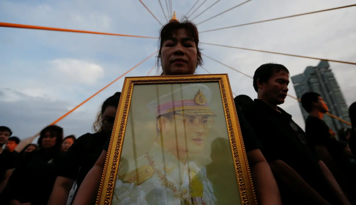 Warga membawa foto Raja Thailand, Bhumibol Adulyadej saat merayakan HUT terakhir almarhum di atas Jembatan Bhumibol, Bangkok, Thailand, Senin (5/12). Raja Bhumibol meninggal di usia 88 tahun. (REUTERS/Jorge Silva)