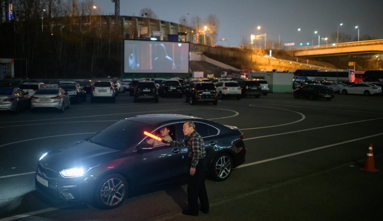 Petugas mengarahkan pelanggan menuju layar film di sebuah bioskop kendara atau drive-in cinema di Seoul, Korea Selatan. Jenis bioskop ini menjadi pilihan yang lebih bagi warga Seoul untuk menikmati film di tengah pandemi virus corona Covid-19 yang mewabah di sejumlah negara. (Ed JONES/AFP)